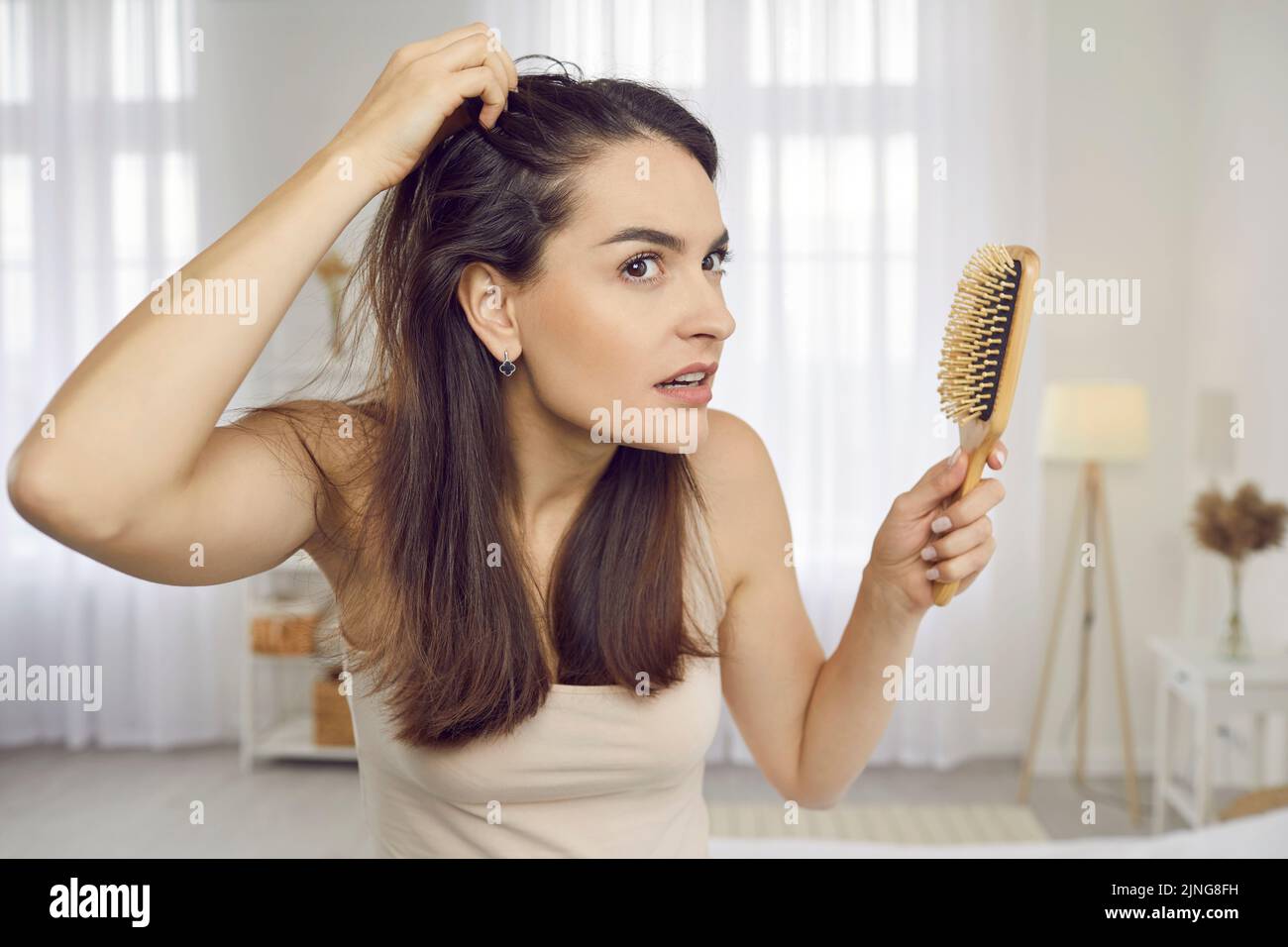 Frau, die durch das Problem des Haarausfalls oder der Kopfschuppenbildung besorgt ist, schaut in den Spiegel Stockfoto