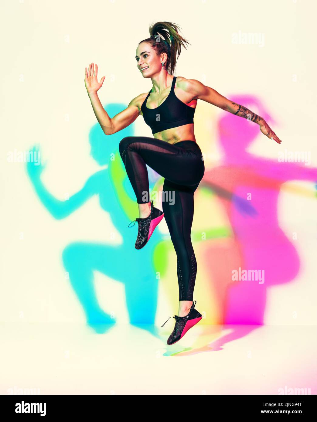 Sportliche Mädchen springen nach oben. Foto von muskulösen Frau in schwarzer Sportkleidung auf weißem Hintergrund mit Effekt von rgb-Farben Schatten. Dynamische Bewegung. Sport Mo Stockfoto