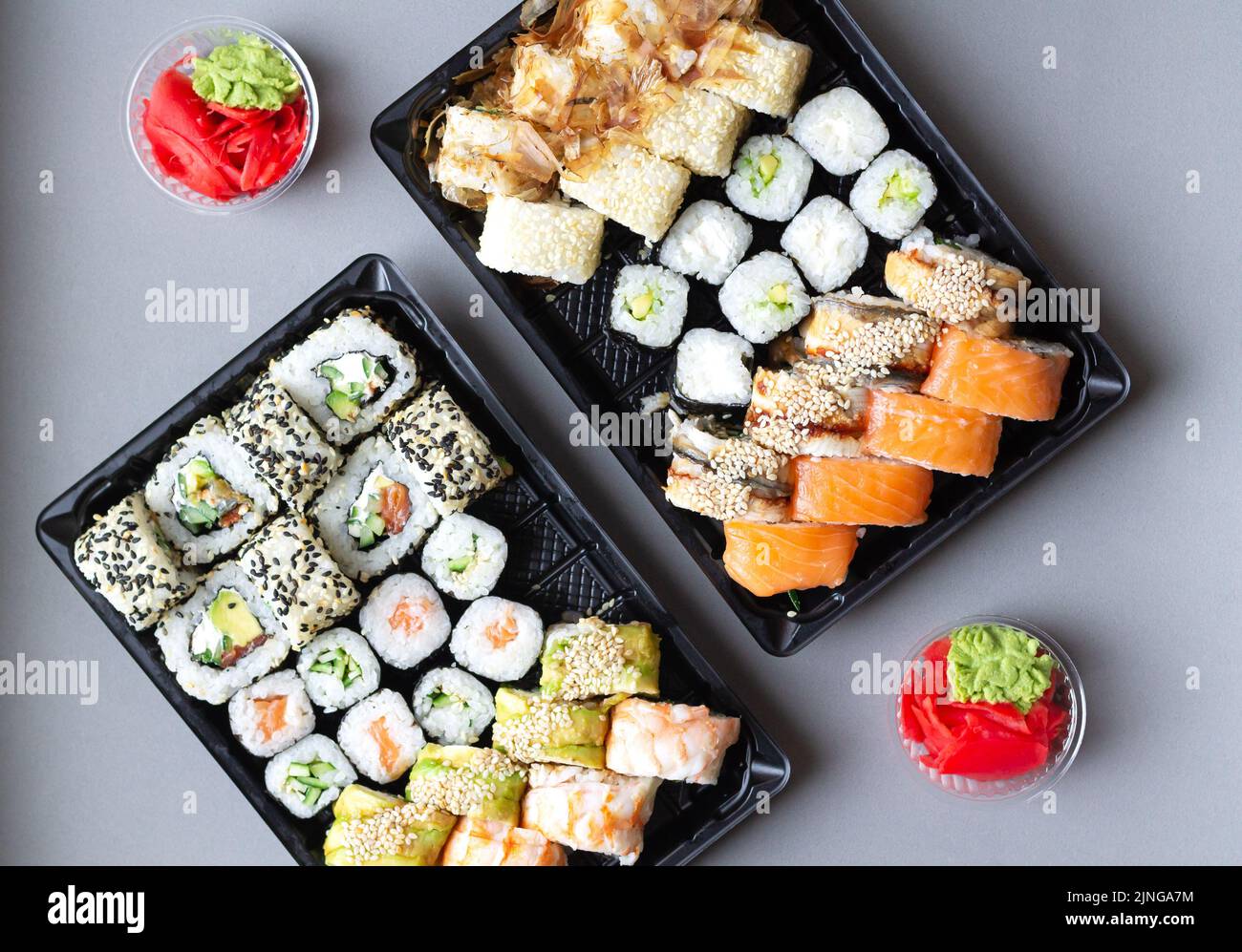 Große Sushi-Rollen in schwarzer Plastikbox zum Mitnehmen auf grauem Hintergrund. Draufsicht Stockfoto