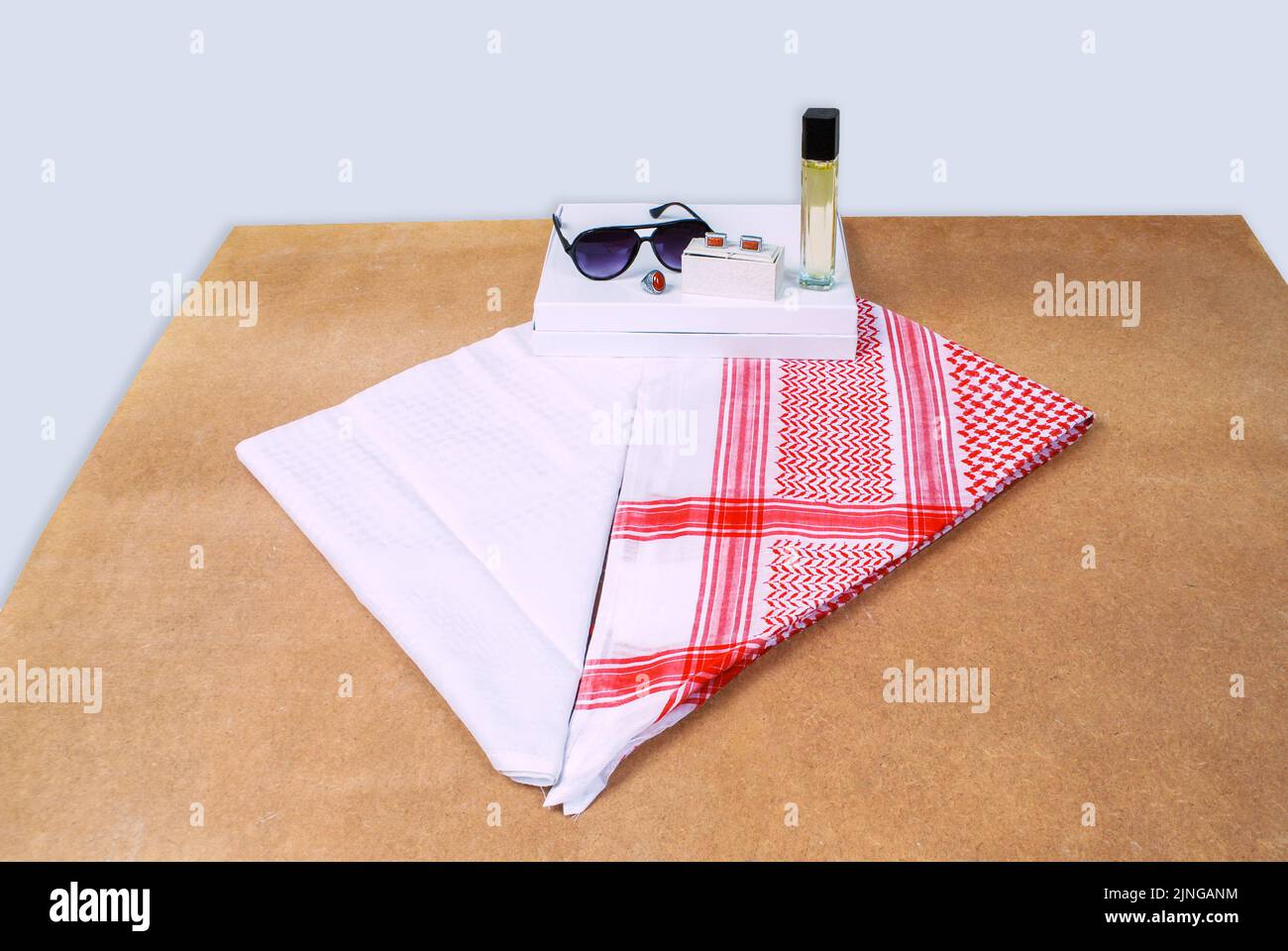Saudi-arabische Männer tragen stilistische Accessoires rot weißes Kopftuch shemagh Sonnenbrille Parfüm Steinring Manschettenknöpfe auf Holzlaken verziert Stockfoto