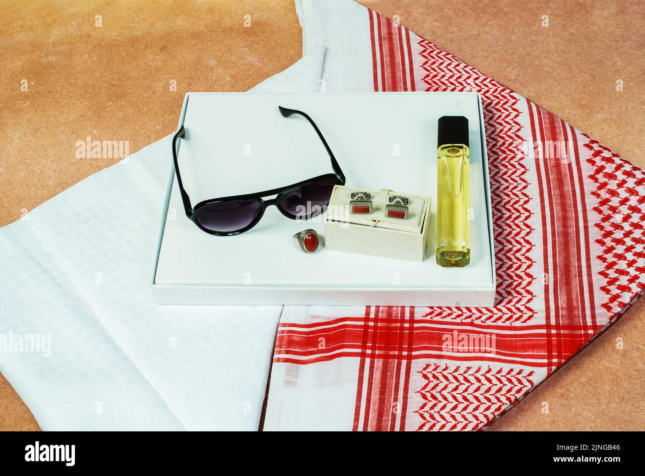 Saudi-arabische Männer tragen stilistische Accessoires rot weißes Kopftuch shemagh Sonnenbrille Parfüm Steinring Manschettenknöpfe auf Holzlaken verziert Stockfoto