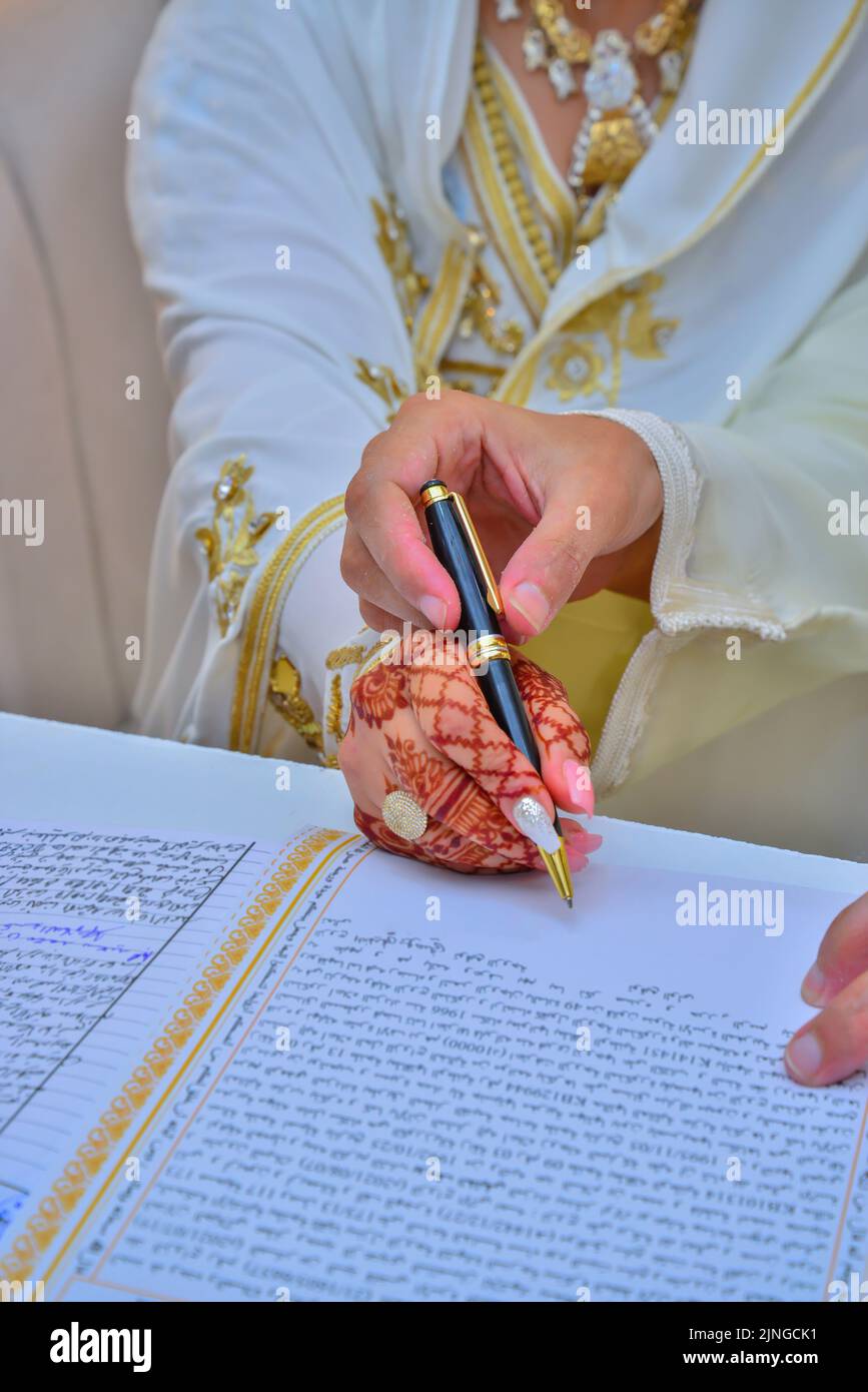 Eine arabische Braut unterzeichnet ihren Ehevertrag mit Henna-Tattoos auf ihren Händen Stockfoto