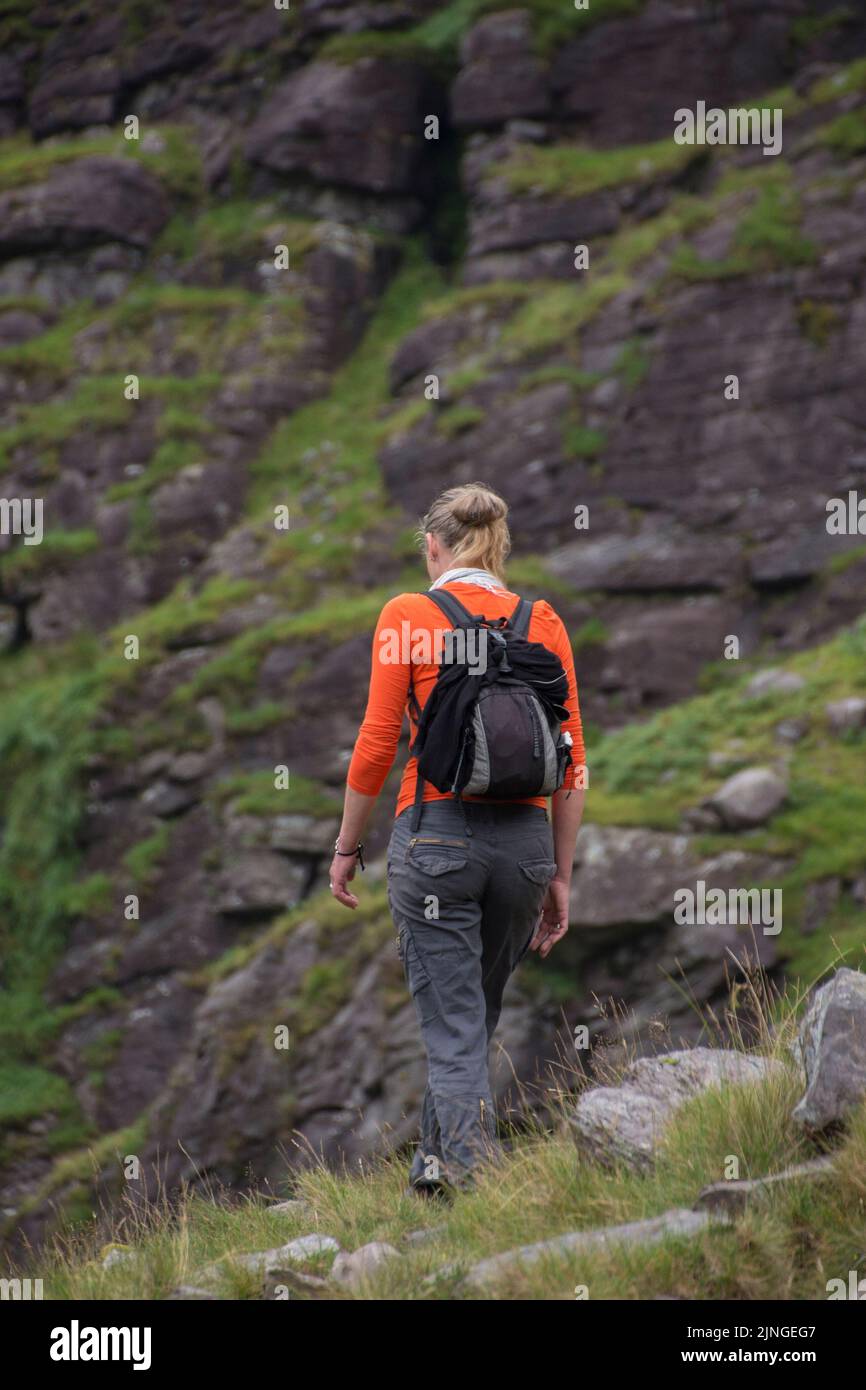 Eine Frau in Orange und ein kleiner Rucksack wandern auf Caurrauntoohil Stockfoto