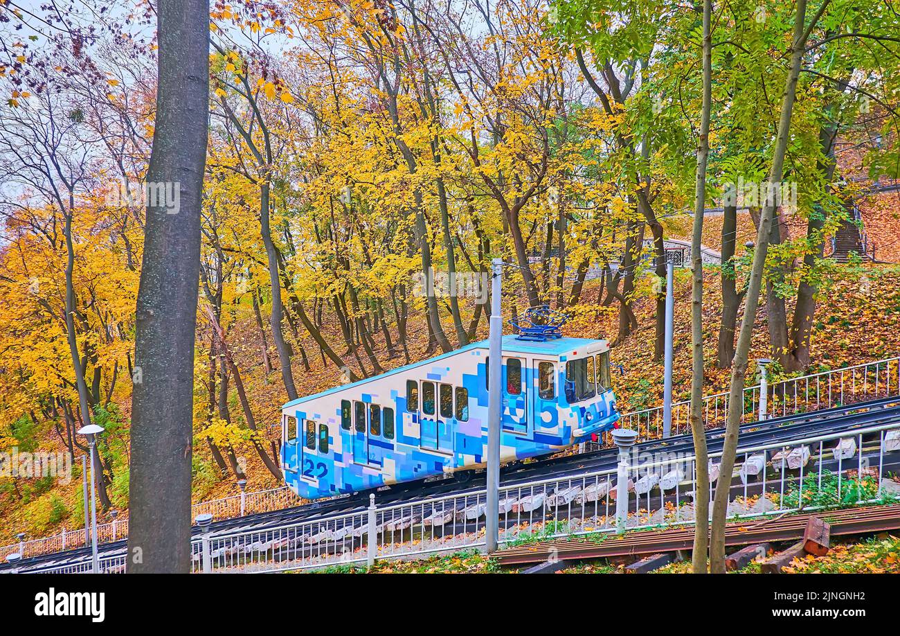 Der leuchtend blaue Wagen der Kiewer Standseilbahn, die entlang des Hügelhangs fährt, bedeckt mit einem gelben Herbstpark des Wolodymyr-Hügels, Kiew, Ukraine Stockfoto