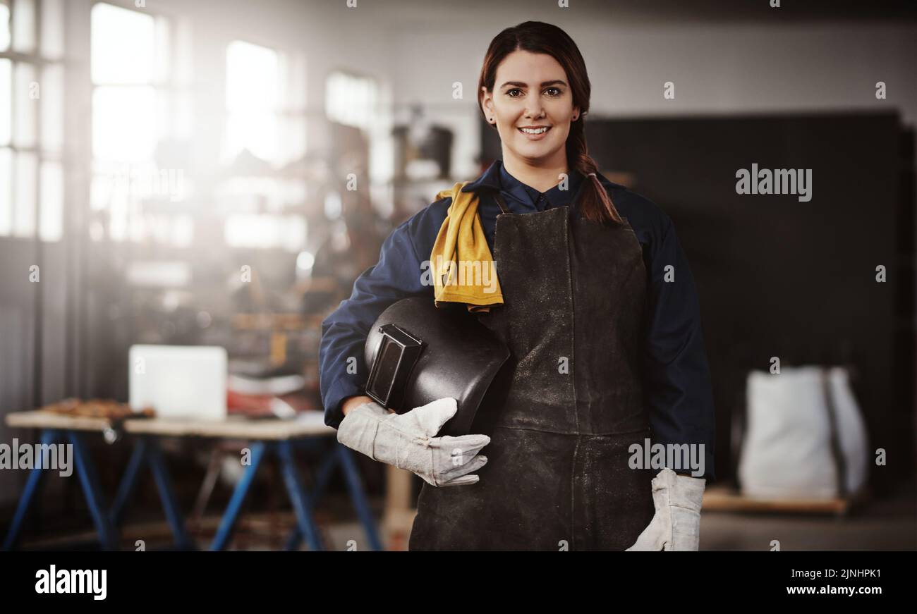 Sicherheit geht vor. Ein Porträt einer attraktiven jungen kreativen Kunsthandwerkerin, die in ihrer Werkstatt steht und ihren Helm unter ihrem Arm versteckt. Stockfoto