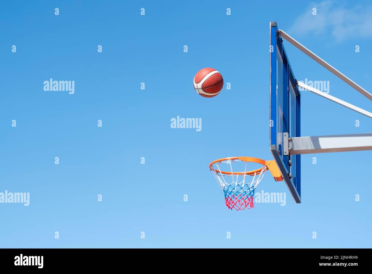 Basketball in einem Netz auf einem blauen Himmel Hintergrund. Der Ball traf den Ring. Sport, Teamspiel. Konzeptionell: Sieg, Erfolg, Zielerreichungen, Sport. Stockfoto