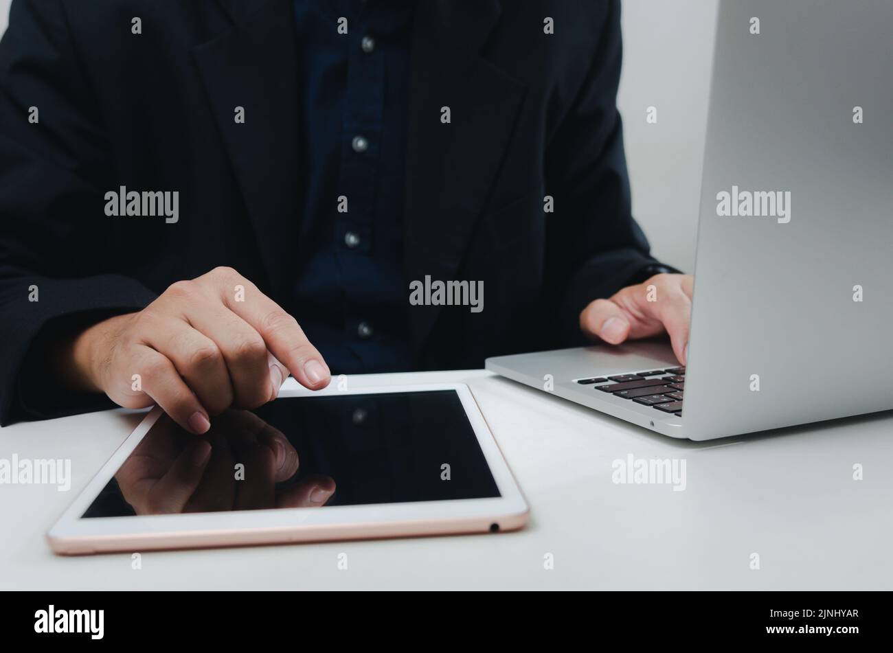Ein Geschäftsmann mit einem Touch-Tablet und einem Laptop sucht mithilfe der Internettechnologie am Schreibtisch nach Informationen. Stockfoto