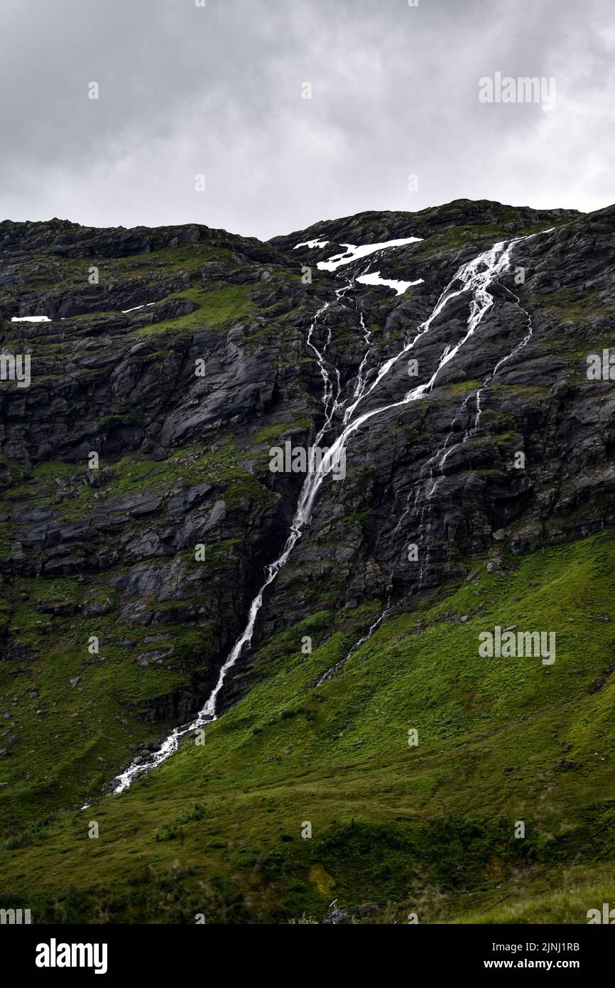 Eine vertikale Aufnahme eines Wasserfalls, der unter einem grau bewölkten Himmel die moosigen Felsen herabfällt Stockfoto