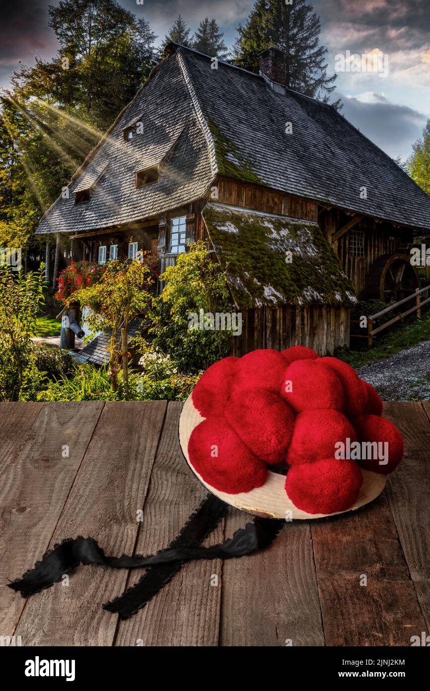 Original Schwarzwälder Bollenhut auf einem Holztisch vor einer historischen Wassermühle Stockfoto