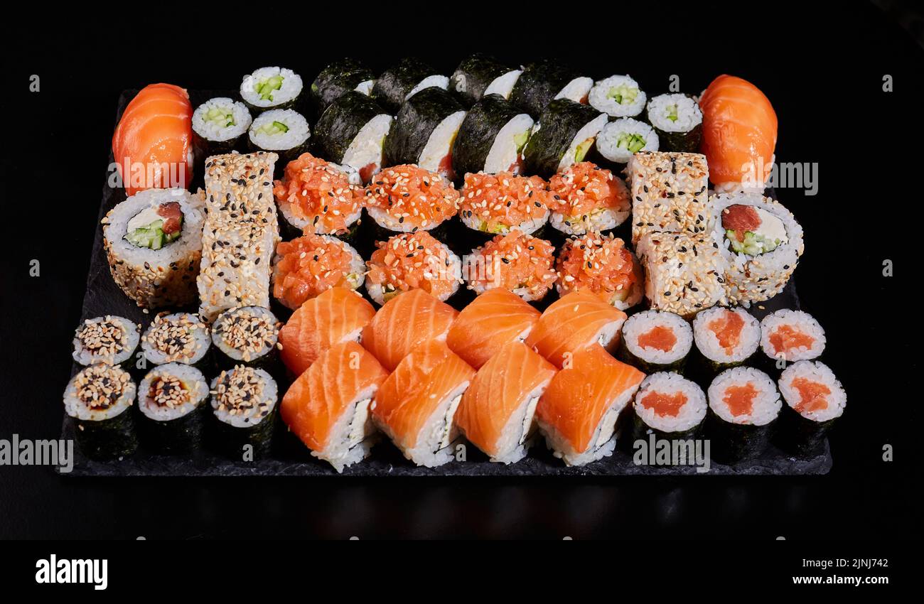 Auswahl an verschiedenen Arten von Sushi-Rollen, die auf einem schwarzen Steinbrett platziert sind. Sushi-Menü mit Nigiri, Maki, Uramaki für die Bestellung in einem Restaurant oder Deli Stockfoto