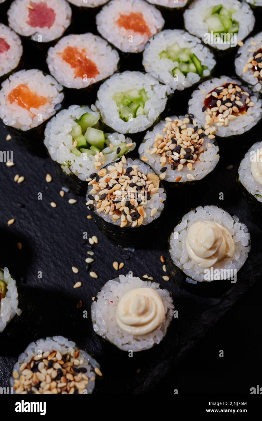 Draufsicht Maki-Brötchen mit Lachs, Thunfisch, Gurkensesame und Frischkäse liegen auf einem Sushi-Brett aus schwarzem Stein. Traditionelle japanische Küche. Stockfoto
