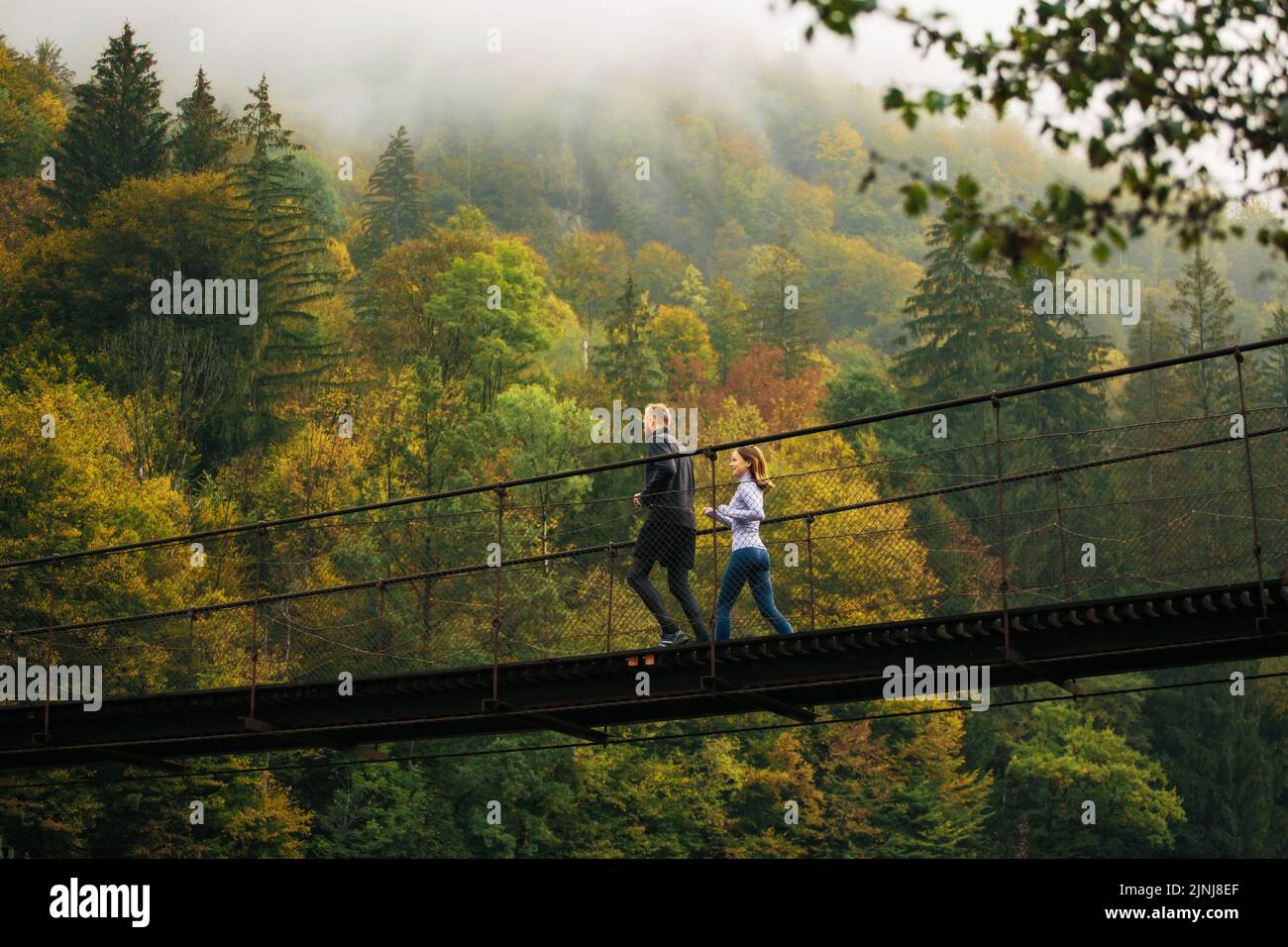 Ein gesunder Lebensstil. Blick von unten auf einen jungen, athletischen Mann und eine junge Frau, die einen Morgenlauf auf einer Hängebrücke vor dem Hintergrund eines ausführen Stockfoto
