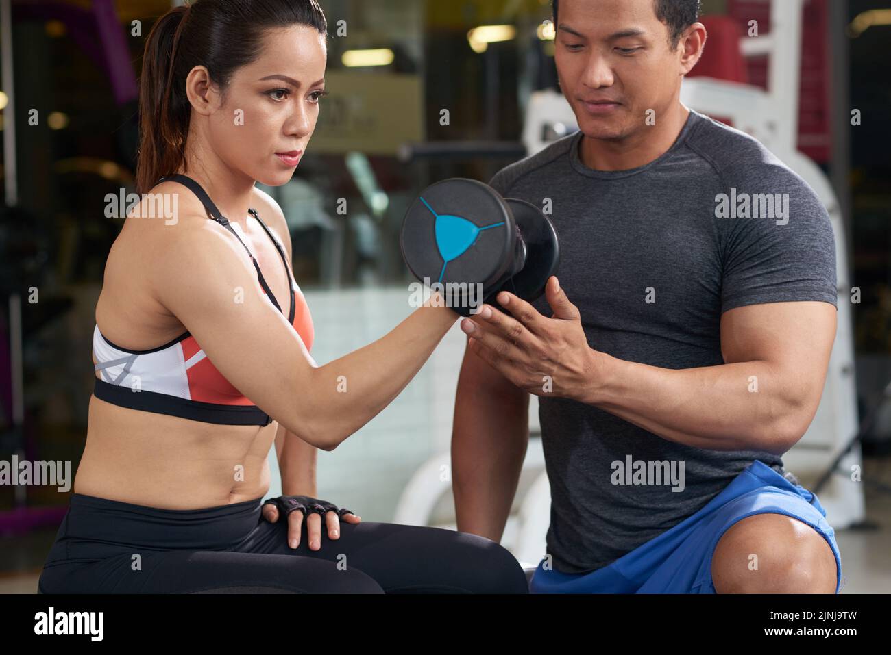 Hübsche vietnamesische Frau, die unter Kontrolle des Fitnesstrainers ihre Arme trainiert Stockfoto
