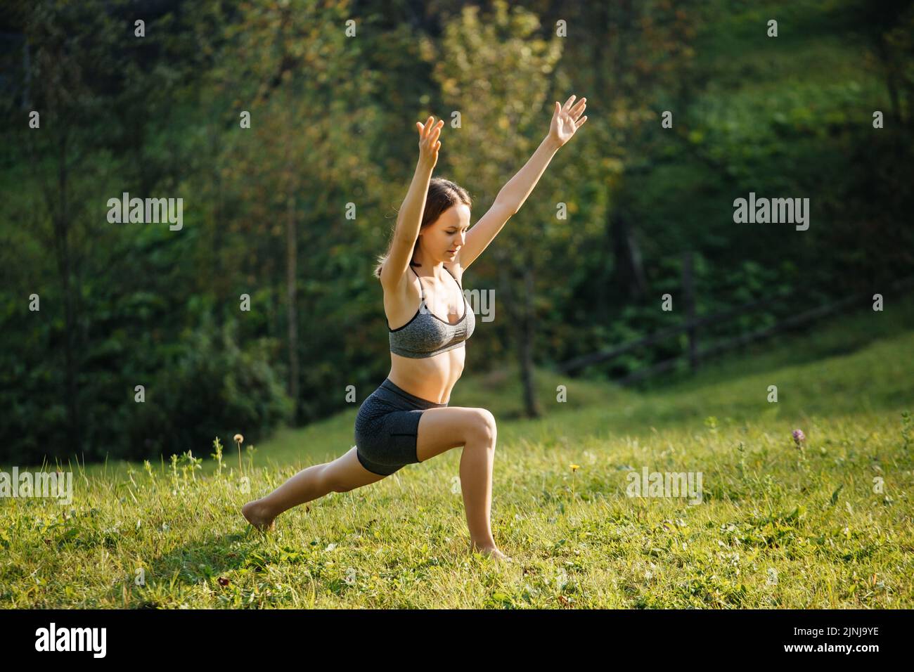 Junge Frau in Sportkleidung, die Yoga und Meditation praktiziert und draußen vor der Stadt Atemübungen macht. Frau trainiert morgens auf dem Gras Stockfoto