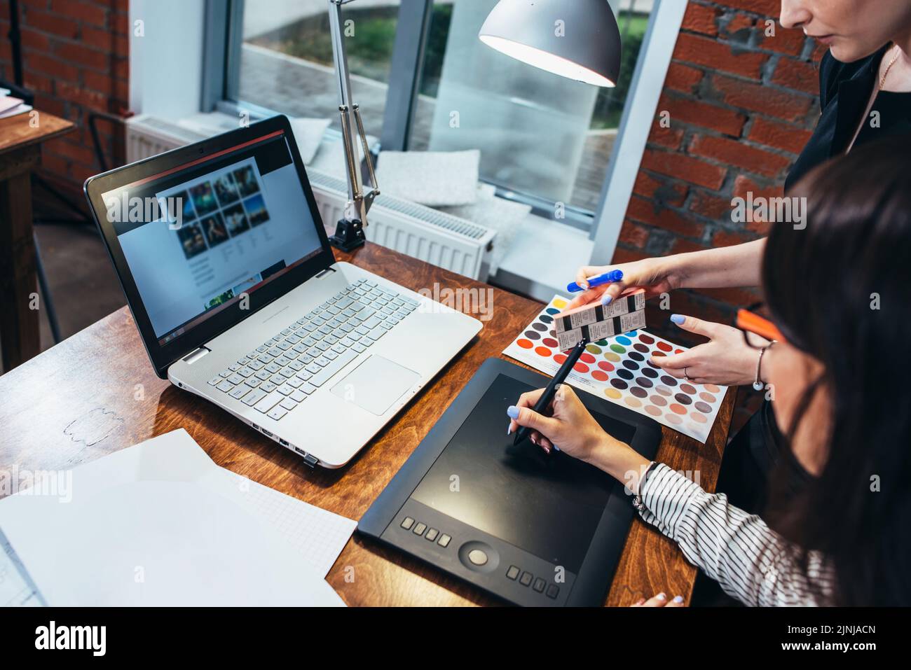 Team von weiblichen Innenarchitekten zeichnet ein neues Projekt mit Grafik-Tablet, Laptop und Farbpalette sitzen am Schreibtisch in modernen Studio. Stockfoto