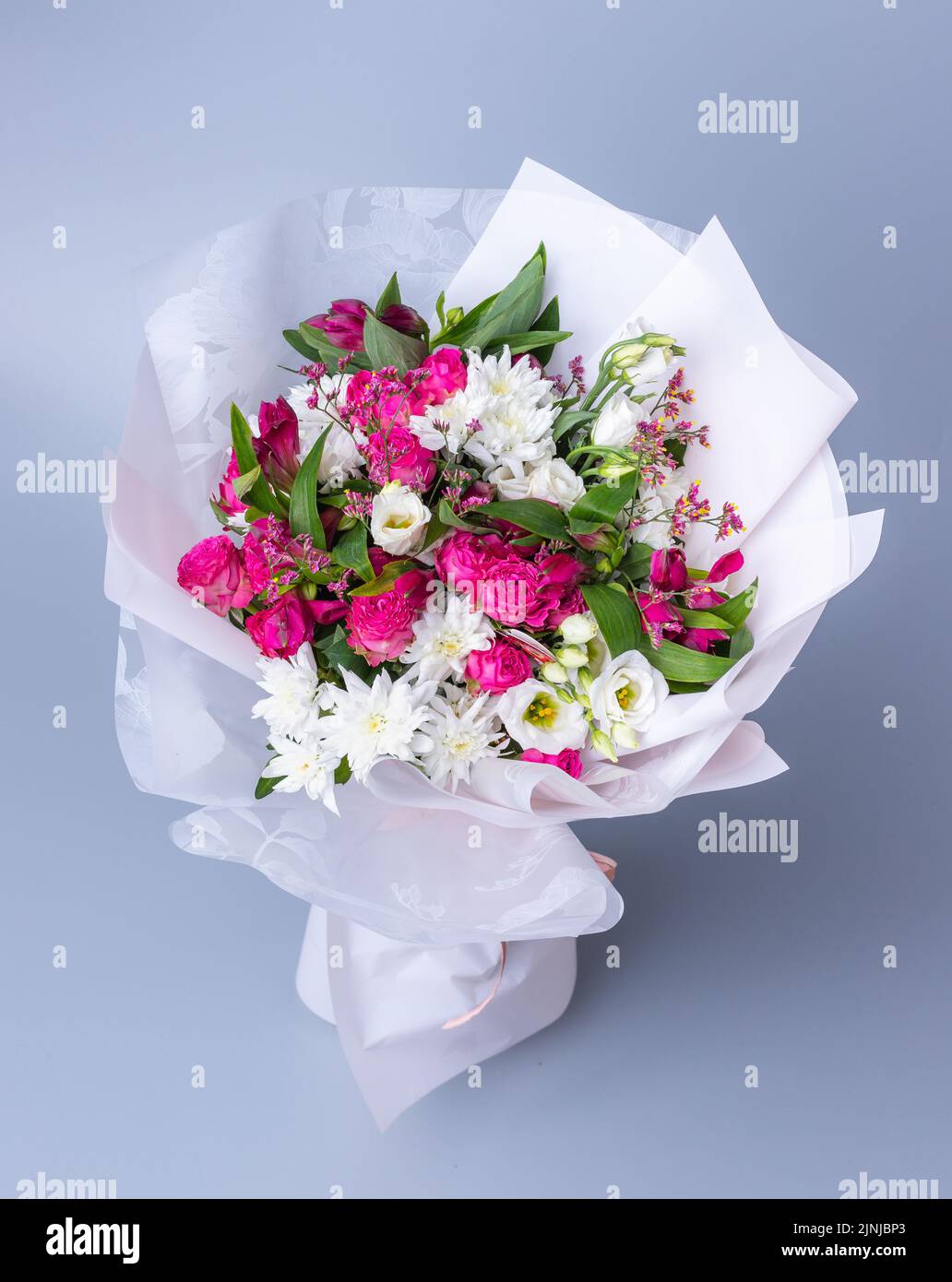 Großer Strauß von rosa und weißen Blumen, eingewickelt in helles Blumenpapier auf blauem Hintergrund. Festlich gepacktes Bouquet mit rosa Pfingstrosen, weißer chrysanth Stockfoto