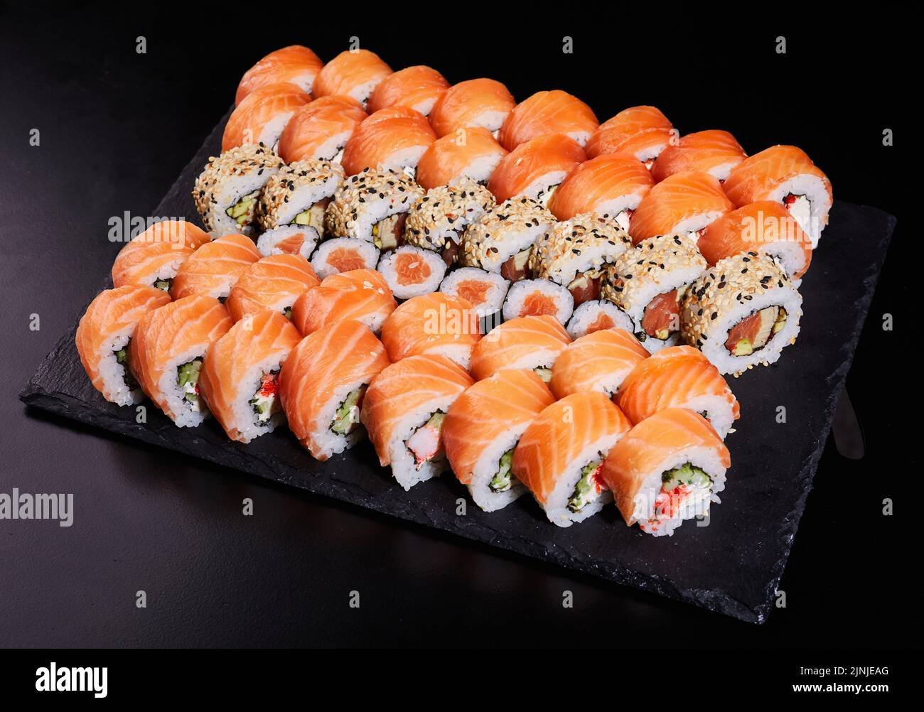 Große Sushi-Rollen, bestehend aus vielen Rollen in Kalifornien und Mackie. Sushi mit frischer Füllung auf einem schwarzen Steinteller. Stockfoto