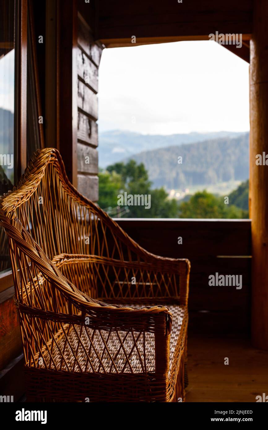 Schöner brauner Korbsessel auf der Terrasse eines Holzhauses mit Blick auf den Bergwald. Unscharfer Hintergrund. Freizeitkonzept. Stockfoto