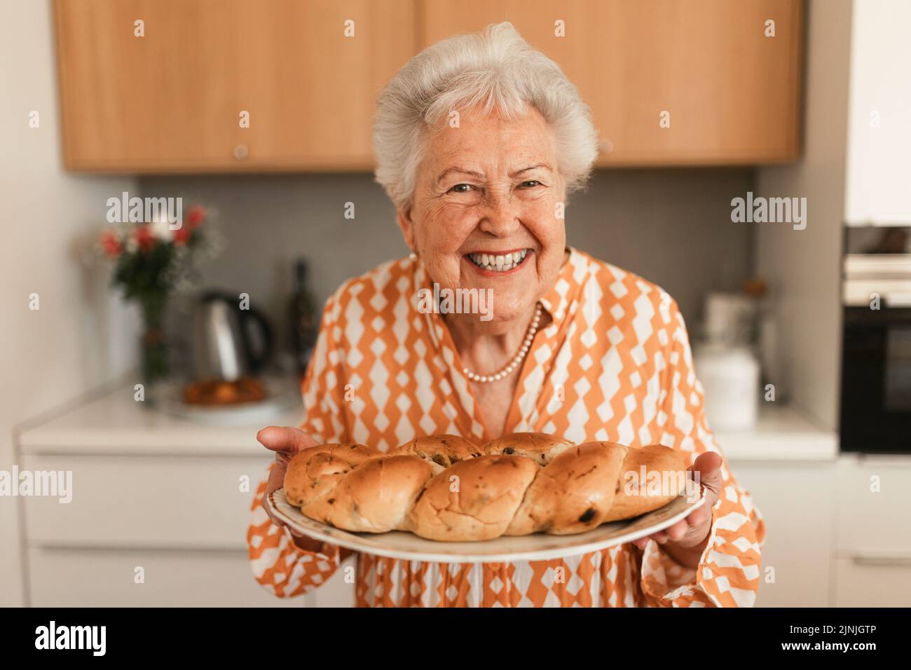 Glückliche ältere Frau mit hausgemachtem süßen geflochtenen Brot mit Rosinen. Stockfoto