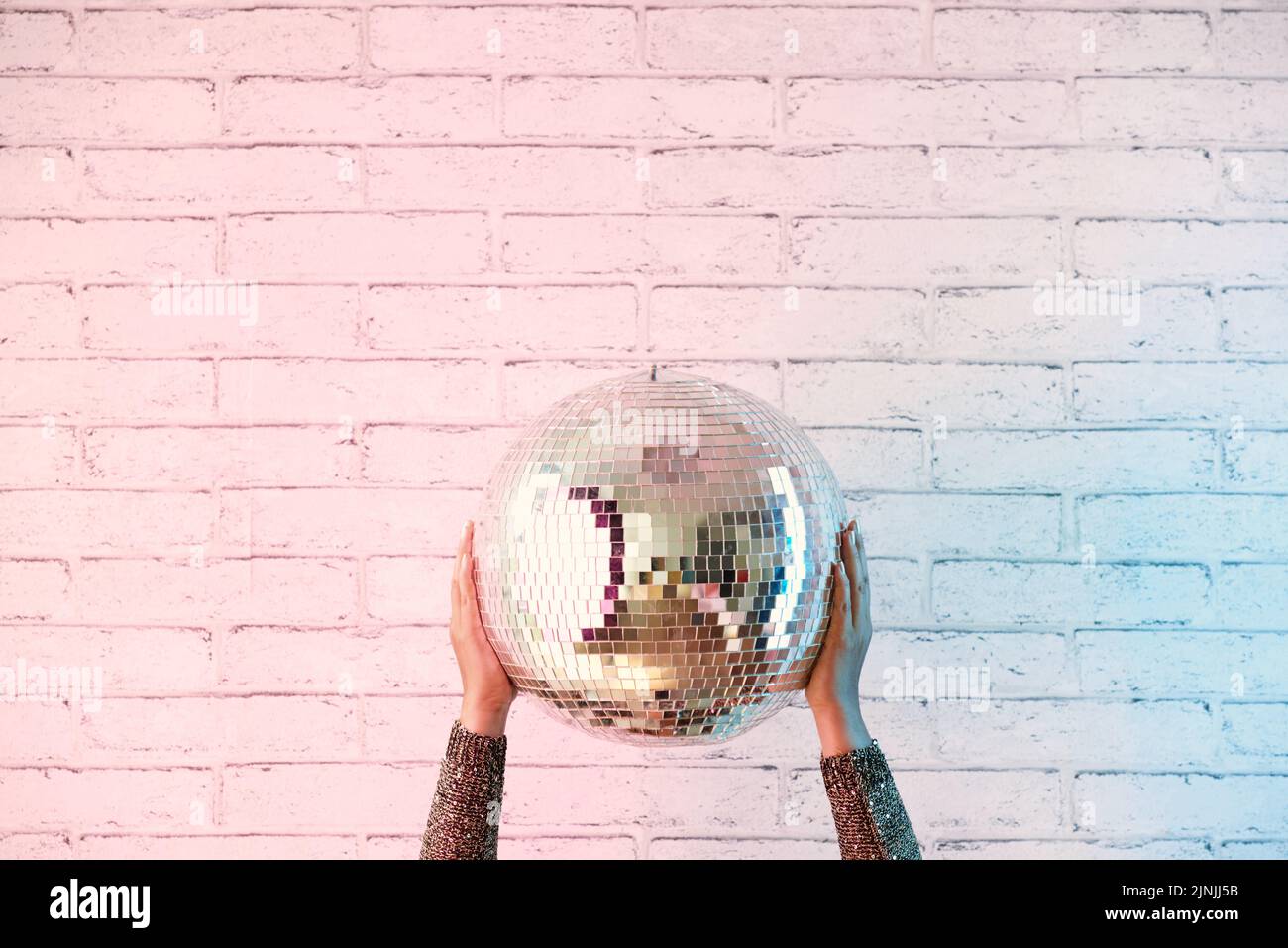 Nahaufnahme der weiblichen Hände mit Disco-Ball, weiße Ziegelwand auf dem Hintergrund, Kopierraum Stockfoto