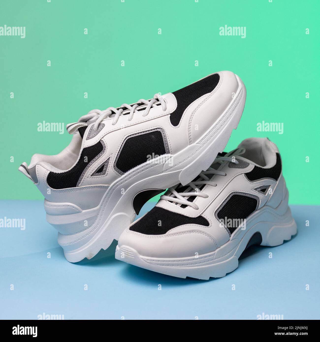 Details. Nahaufnahme von schwarz-weißen Sportschuhen auf farbigem Hintergrund. Ein Sneaker ruht auf einem anderen, der auf blauem und grünem Hintergrund steht. Sport-Sh Stockfoto