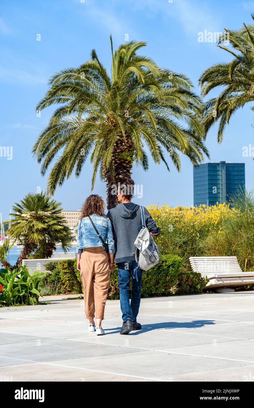 Ein Blick auf ein wunderschönes Paar, das an einem sonnigen Tag in einem Park mit Palmen spazieren geht Stockfoto