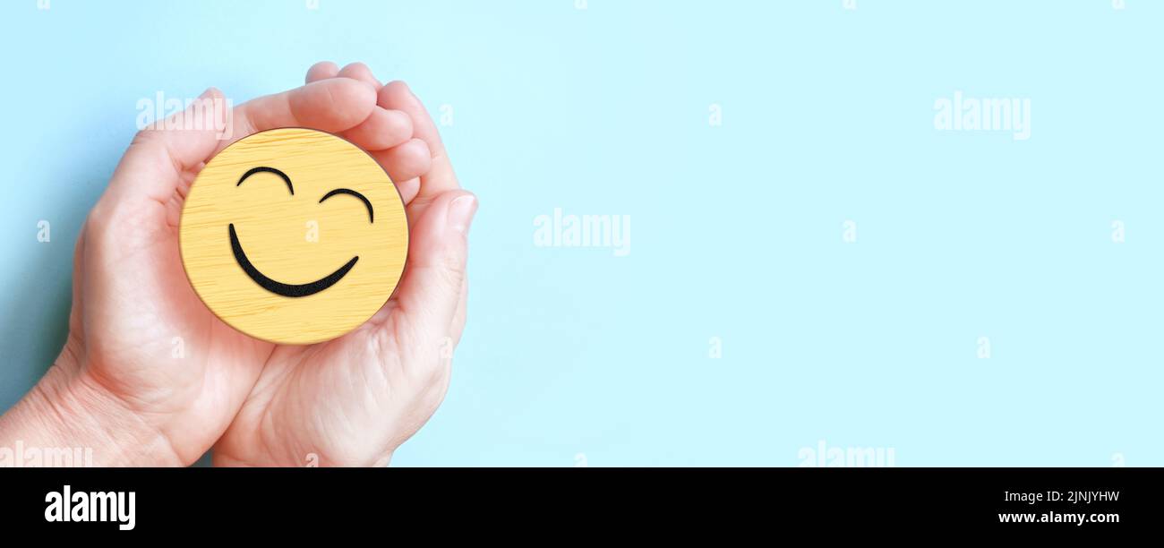 Hand hält glückliches Lächeln Gesicht auf blauem Hintergrund, positives Denken, psychische Gesundheit, Welt psychische Gesundheit Tag Konzept Stockfoto