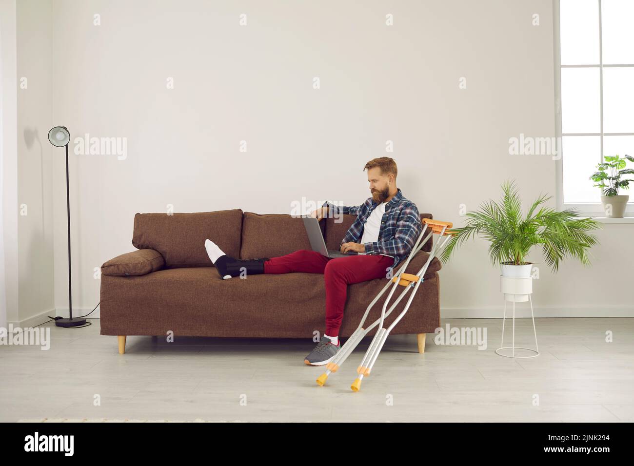 Ein Mann mit Beinverletzung verwendet einen Laptop, um von zu Hause aus zu arbeiten, Filme anzusehen, im Internet zu suchen und die Lieferung zu bestellen. Stockfoto