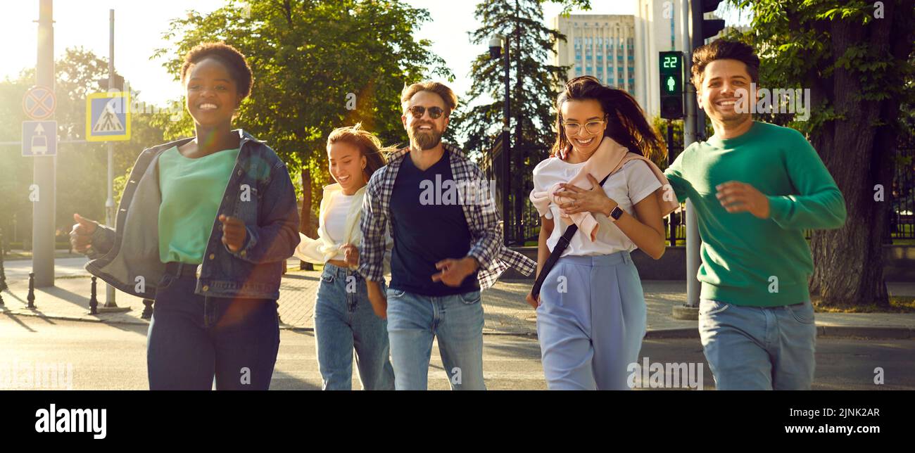 Fröhliche Gruppe von Freunden, die durch die Stadt laufen und über die Straße an der grünen Ampel laufen. Stockfoto