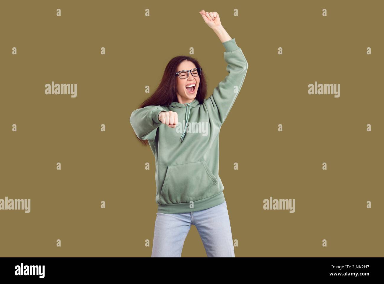 Fröhliche, verrückte, fröhliche junge Frau, die ihren Erfolg feiert, indem sie auf khaki-Hintergrund tanzt. Stockfoto