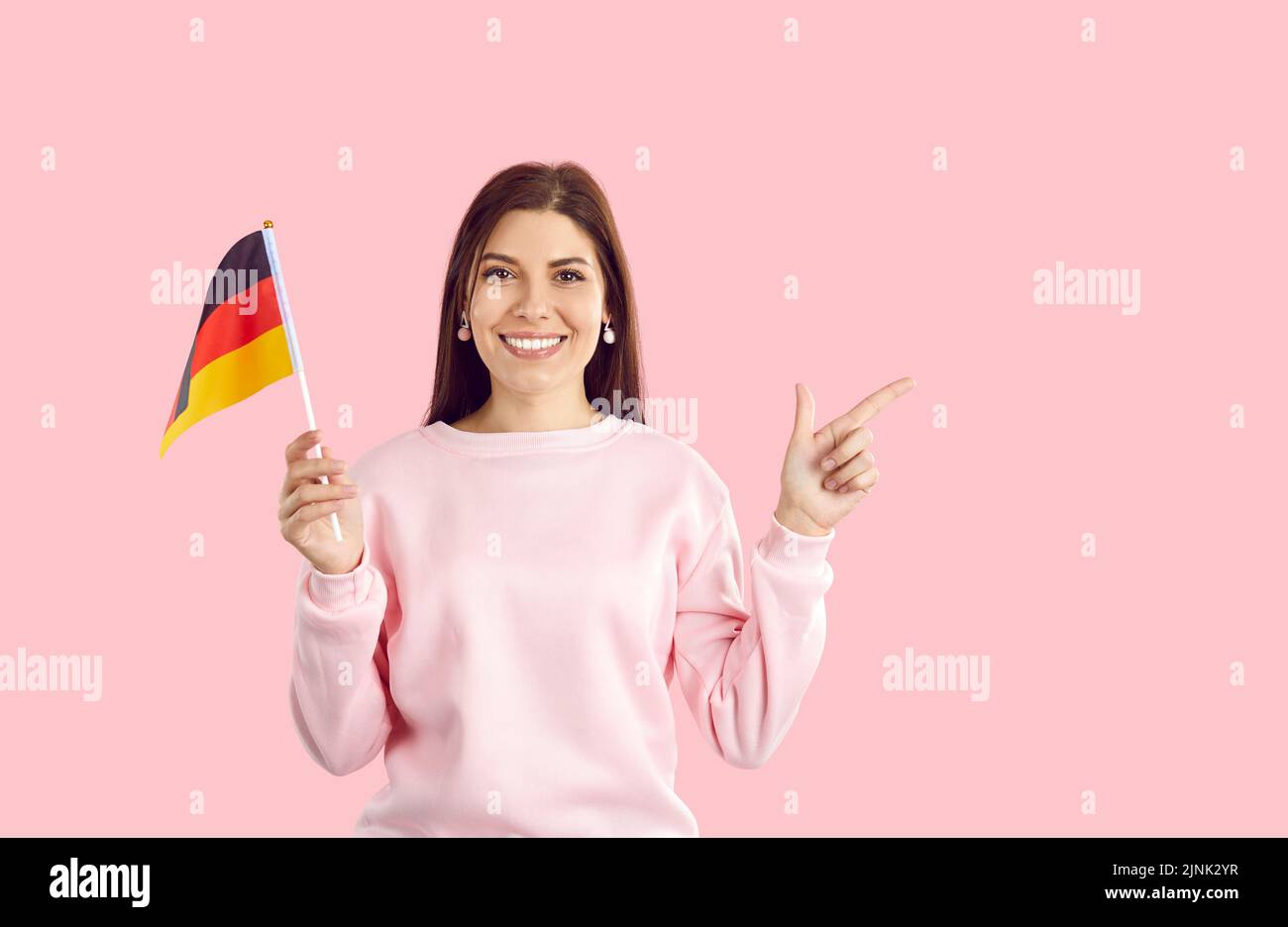 Glückliche Frau isoliert auf rosa Hintergrund hält deutsche Flagge, zeigt auf den Kopierraum und lächelt Stockfoto