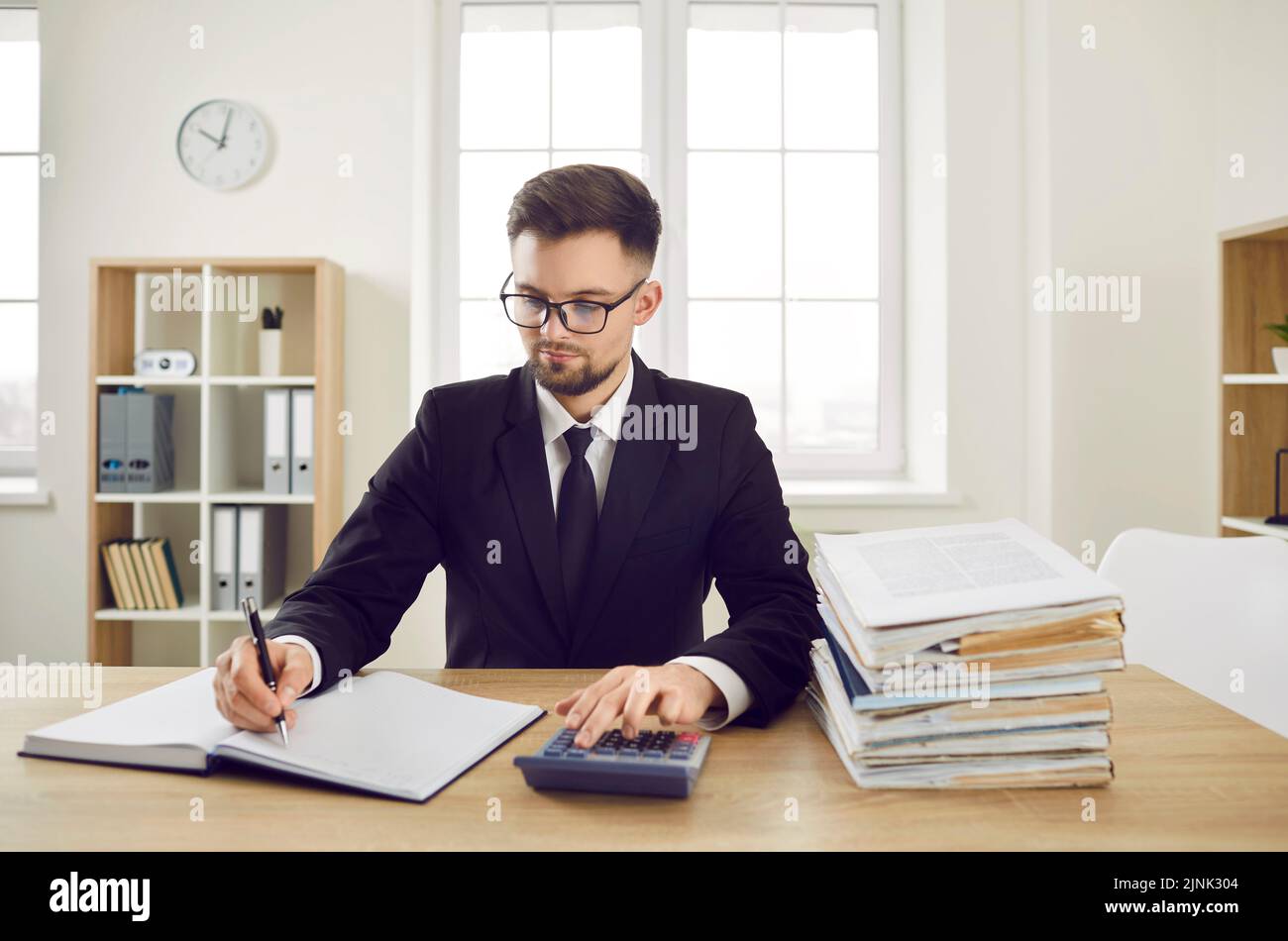 Buchhalter sitzt am Schreibtisch, arbeitet mit Firmendokumenten und verwendet Taschenrechner Stockfoto