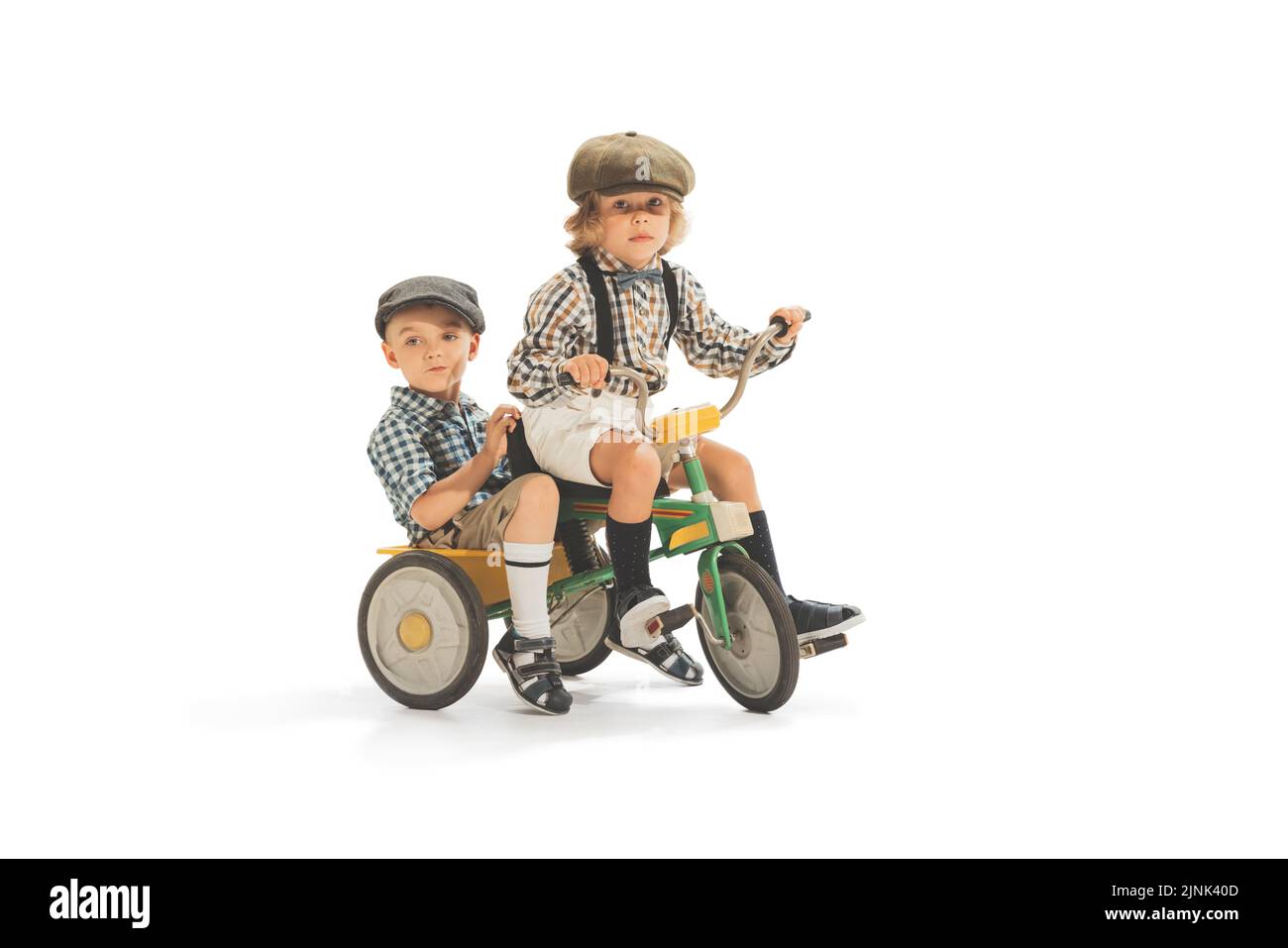 Nette glückliche Kinder Reiten Dreirad isoliert auf weißem Studio Hintergrund. Retro-Vintage-Stil-Konzept. Freundschaft, Hobbys, Kunst, Epochenvergleich Stockfoto