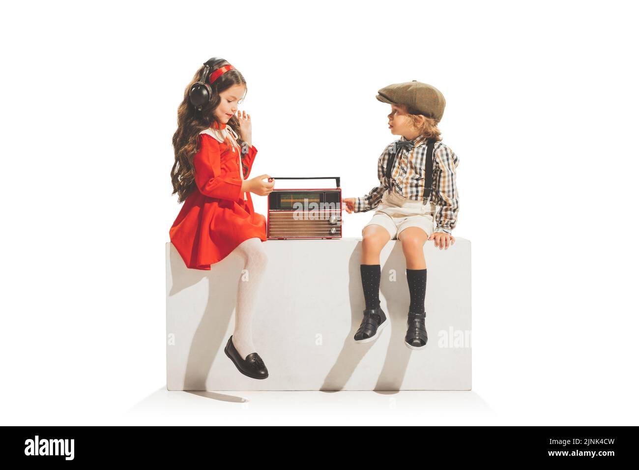 Nette glückliche Kinder sitzen und Musik hören isoliert auf weißem Hintergrund. Retro-Vintage-Stil-Konzept. Freundschaft, Hobbys, Kunst, Epochenvergleich Stockfoto