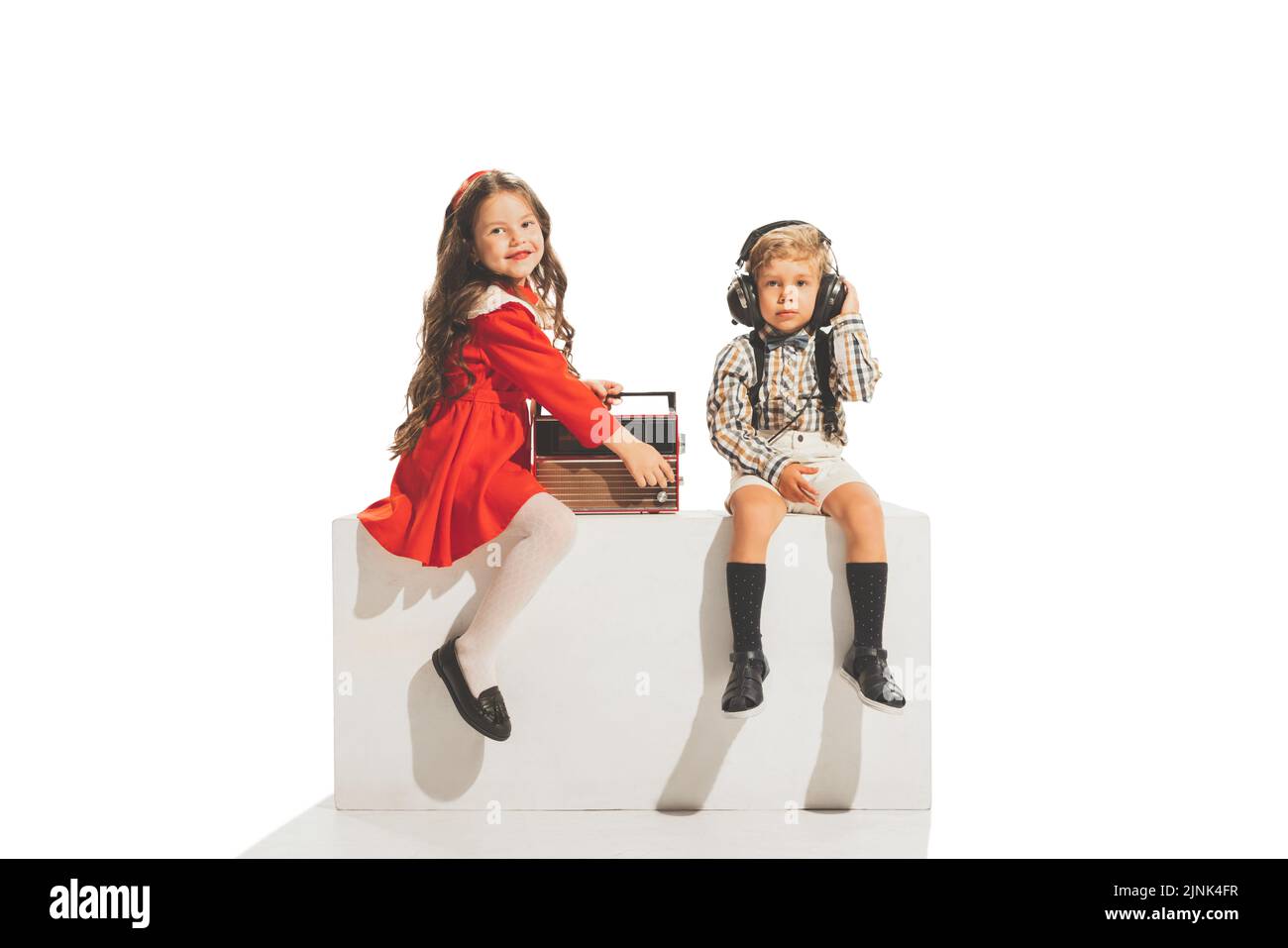 Nette glückliche Kinder sitzen und Musik hören isoliert auf weißem Hintergrund. Retro-Vintage-Stil-Konzept. Freundschaft, Hobbys, Kunst, Epochenvergleich Stockfoto