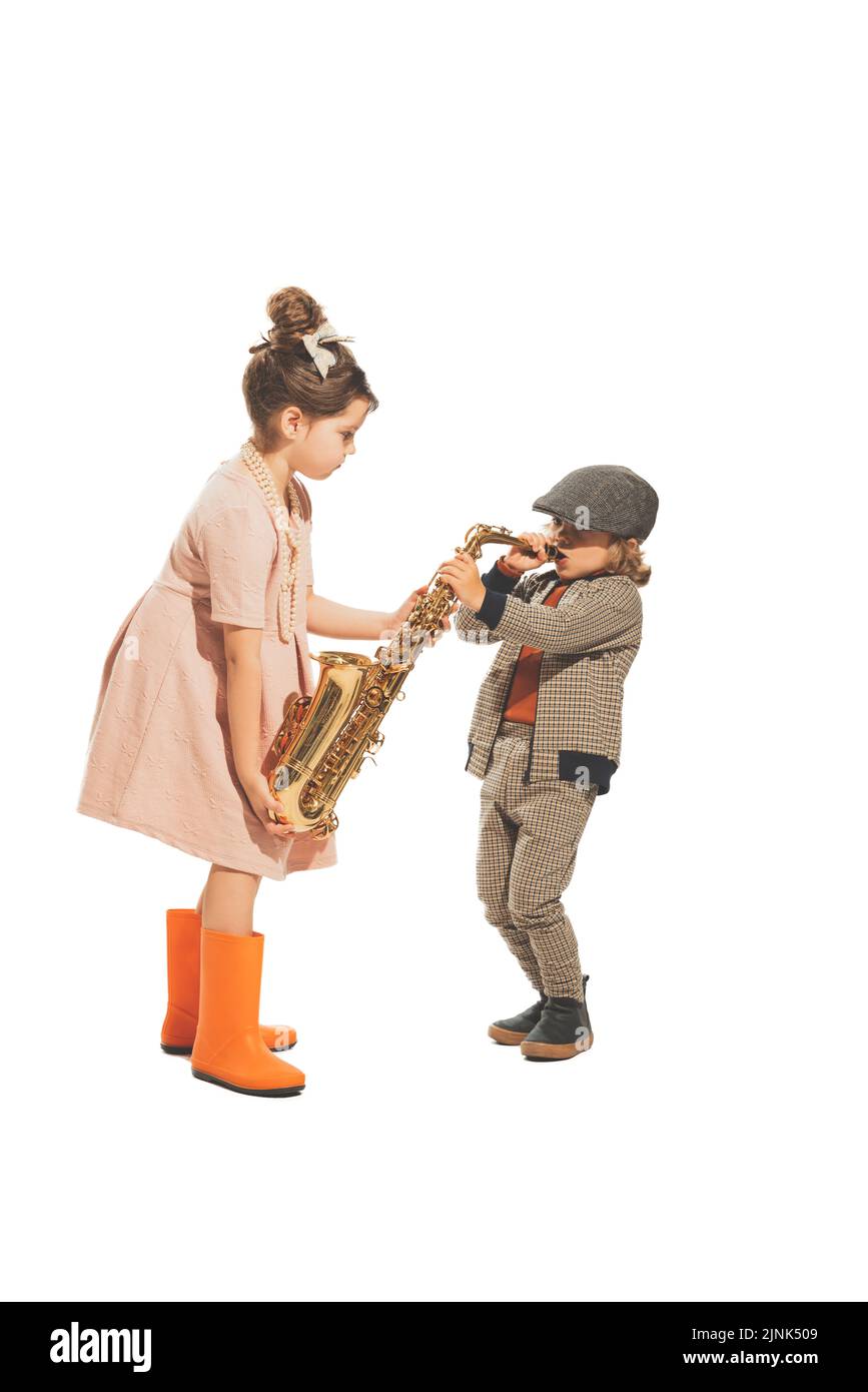 Nette glückliche Kinder spielen mit Saxophon isoliert auf weißem Studiohintergrund. Retro-Vintage-Stil-Konzept. Freundschaft, Hobbys, Kunst, Epochenvergleich Stockfoto