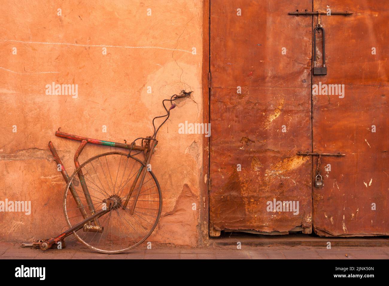 In Marrakesch, Marokko, wurden Reste des Fahrrads an der Wand neben einer rostigen Tür befestigt Stockfoto