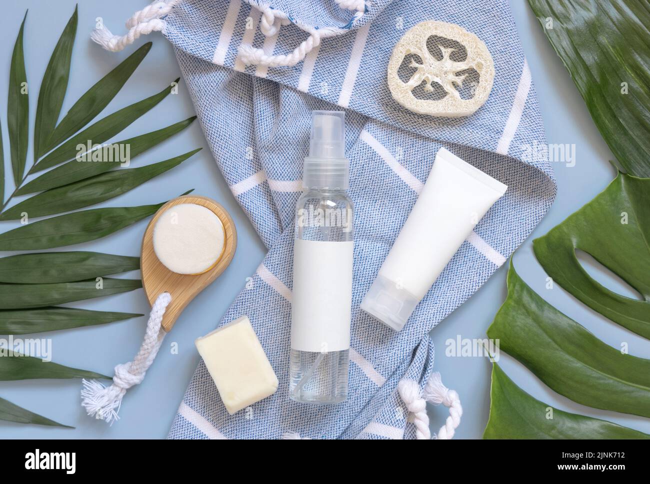 Transparente, wiederfüllbare Sprühflasche und weiße Cremetöhre auf blauem Badetuch in der Nähe von Körperpflegezubehör Draufsicht, Kopierraum. Verpackung mocku Stockfoto