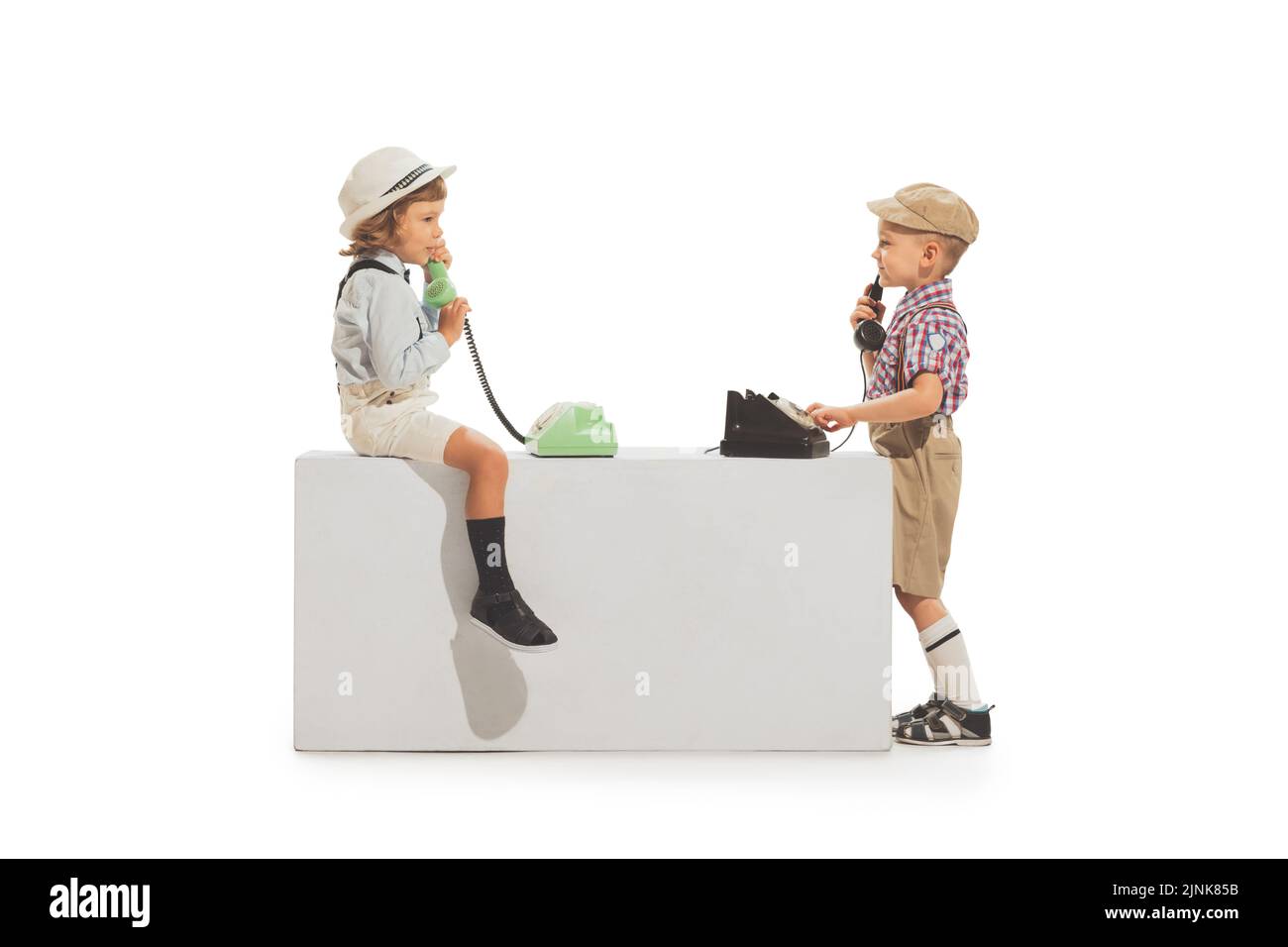 Porträt von zwei fröhlichen Kindern im Retro-Stil Sommer-Outfit mit Vintage-Telefon isoliert auf weißem Hintergrund. Konzept von Kunst, Freundschaft, Hoffnung, Jugend Stockfoto