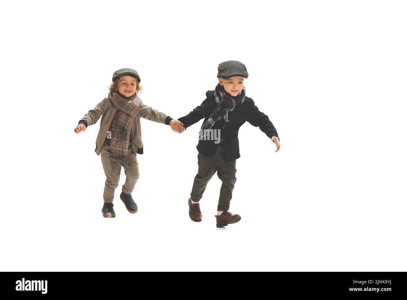 Zwei Jungen im Vorschulalter, modische Kinder in herbstlicher Retro-Kleidung, die isoliert auf weißem Hintergrund spazieren. Konzept der Kindheit, Vintage-Mode Stockfoto
