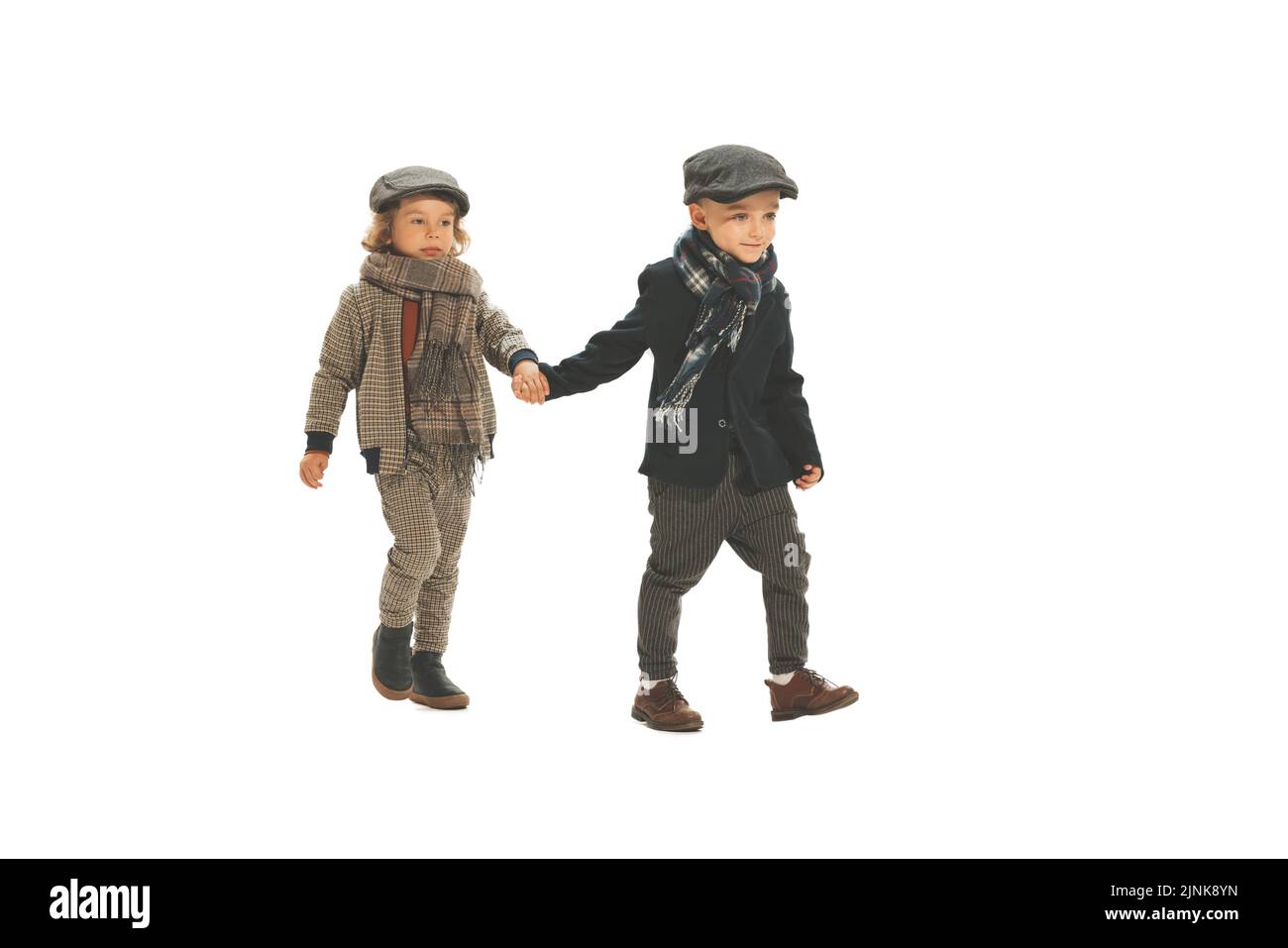 Zwei Jungen im Vorschulalter, modische Kinder in herbstlicher Retro-Kleidung, die isoliert auf weißem Hintergrund spazieren. Konzept der Kindheit, Vintage-Mode Stockfoto