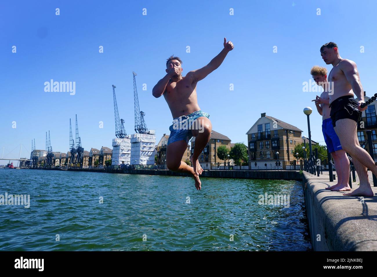 Ein junger Mann posiert, als er in das Royal Victoria Dock im Osten Londons springt. Für einige Teile Englands wird am Freitag eine Dürre ausgerufen, wobei die Temperaturen bis 35C Grad erreichen werden, was das Land heißer macht als Teile der Karibik. Bilddatum: Freitag, 12. August 2022. Stockfoto
