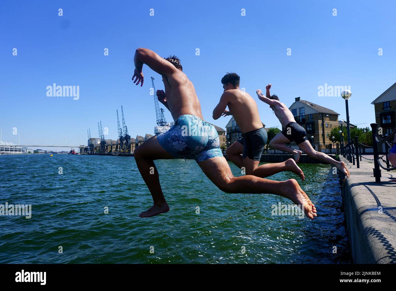 Drei junge Männer springen in das Royal Victoria Dock im Osten Londons. Für einige Teile Englands wird am Freitag eine Dürre ausgerufen, wobei die Temperaturen bis 35C Grad erreichen werden, was das Land heißer macht als Teile der Karibik. Bilddatum: Freitag, 12. August 2022. Stockfoto