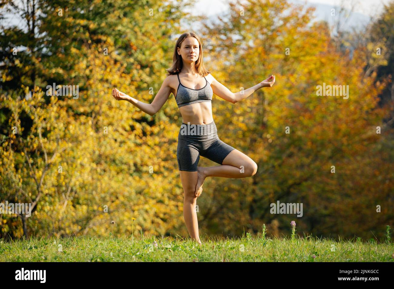 Die junge schlanke Frau steht barfuß auf einem Bein und übt das Balancieren mit Yoga-Atemübungen. Frau meditiert in der Natur in einem ruhigen Berg vi Stockfoto