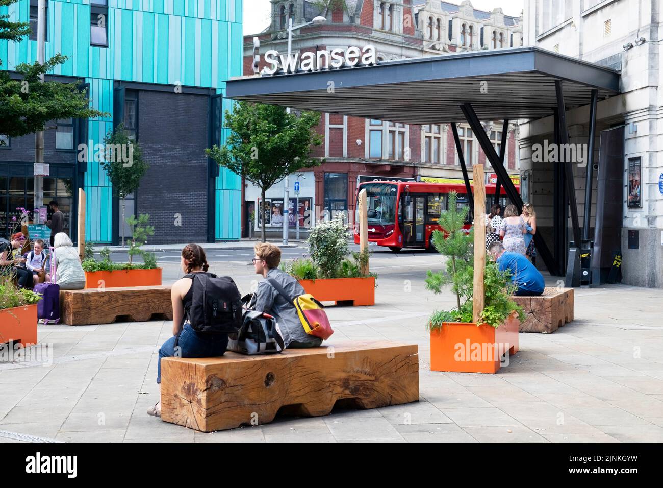 Menschen, die auf Holzbänken sitzen, sitzen vor dem Bahnhof Swansea und unterschreiben am Eingang in Wales UK KATHY DEWITT Stockfoto