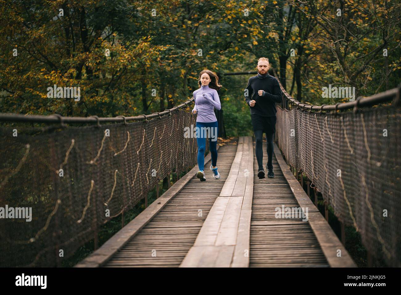 Liebende junge Sportlerpaare laufen an einem kühlen Herbsttag auf einer alten Hängebrücke. Stockfoto