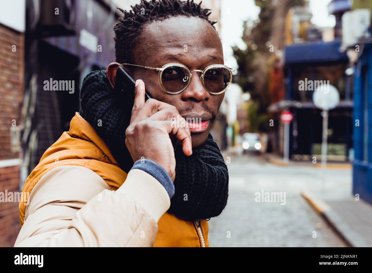 Junger schwarzer Mann afrikanischer Ethnie, dreht sich auf der Straße um, um am Telefon zu sprechen Stockfoto