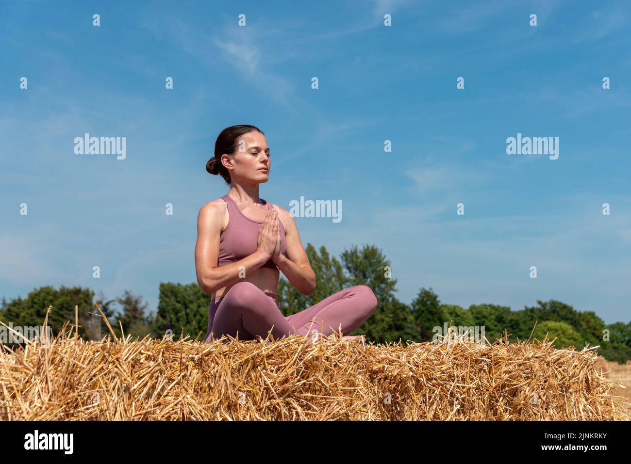 Frau, die auf einem Heuballen auf dem Land sitzt und meditiert. Yoga-Konzept. Stockfoto