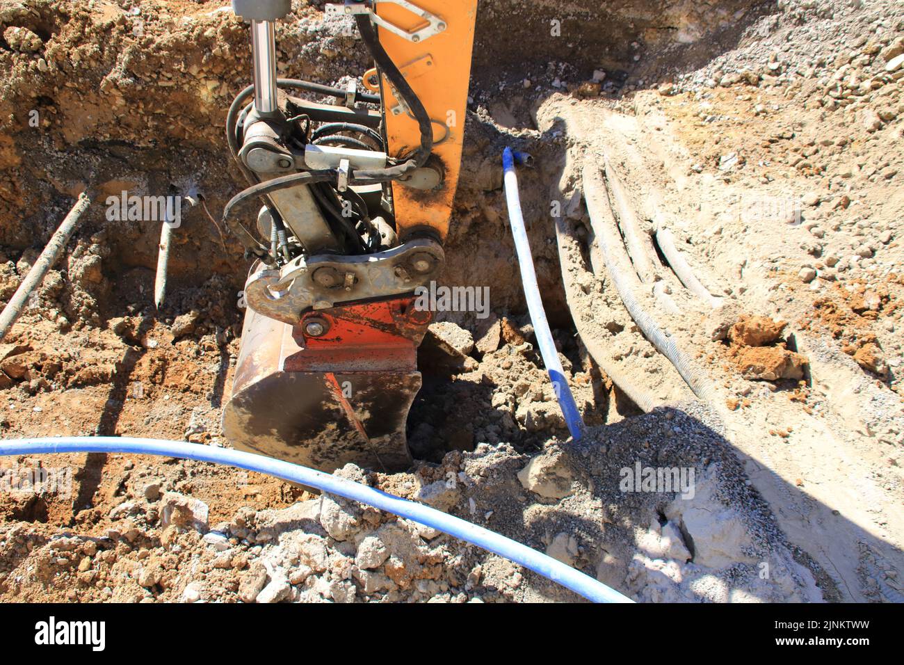 Der Griff eines Baggers gräbt sich neben einem Kabel in den Boden Stockfoto