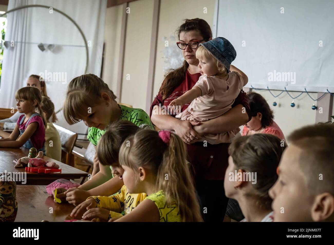 Eine Mutter hält ihr Baby, während sie an einem Kindergottesdienst in einer katholischen Kirche in Slowjansk, Donbas, teilnimmt. Obwohl die Stadt ständig stark von russischen Artillerien und Raketen bombardiert wird, planen einige Bewohner immer noch, in der Stadt Slowjansk zu bleiben, die eine Bevölkerung von 106.972 (2021 estens.) hatte, die heute als eine der wichtigsten strategischen Städte in der Donezker Region im Donbass gilt. Seit Kriegsbeginn wurden über 80 % der Zivilbevölkerung aus dem Krieg evakuiert. Stockfoto